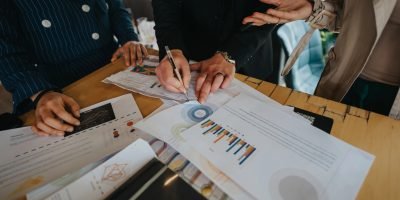 Team members collaborate on a business project, discussing data charts and graphs in a modern office setting.